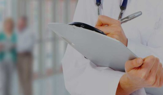 Medical doctor holding clipboard in right hand while writing notes with left hand