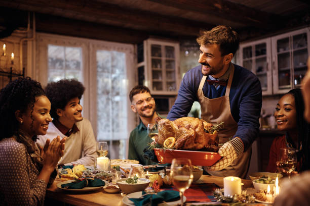 Happy man serving roasted turkey during Thanksgiving dinner with friends at the dining table.